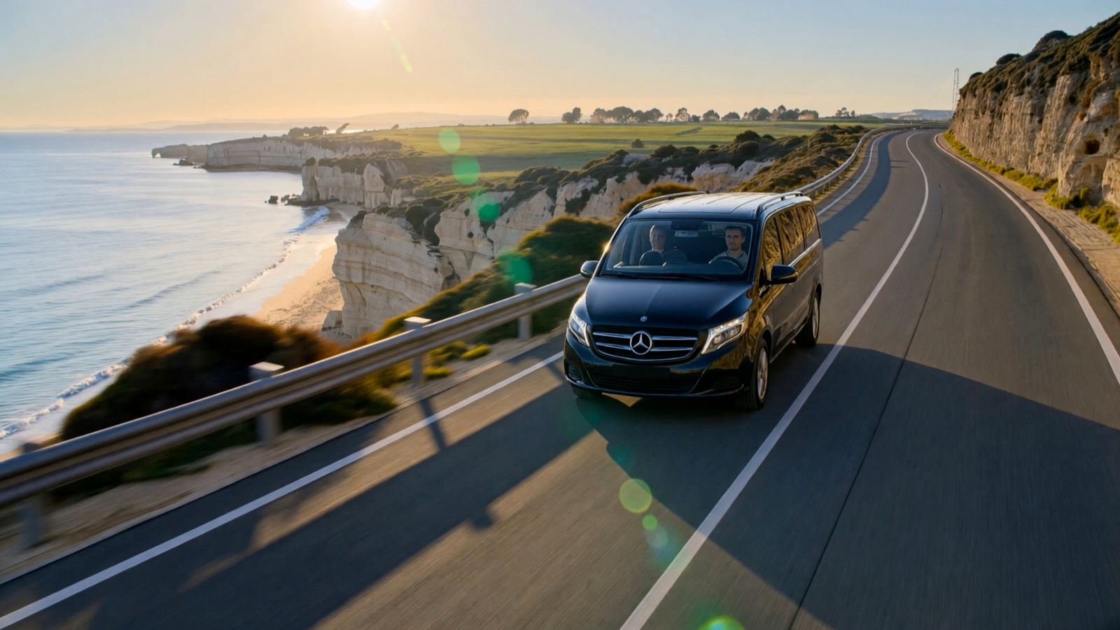 Black Mercedes V-Class driving along a coastal road above an Algarve beach at golden hour